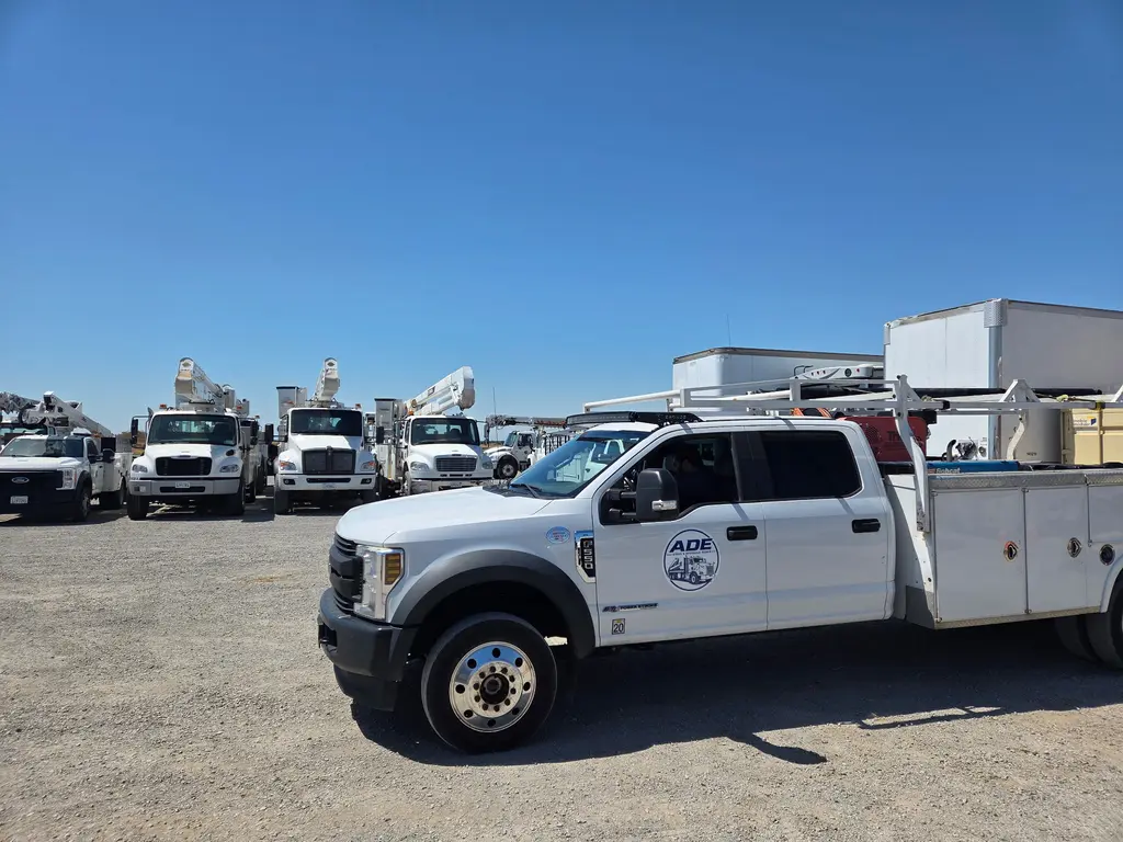 ADE service truck in a utility fleet yard with a row of bucket trucks behind it