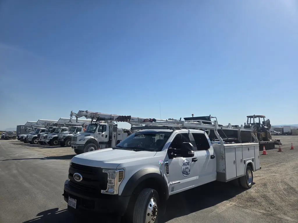 ADE service truck parked in a utility fleet yard with bucket trucks and digger derricks