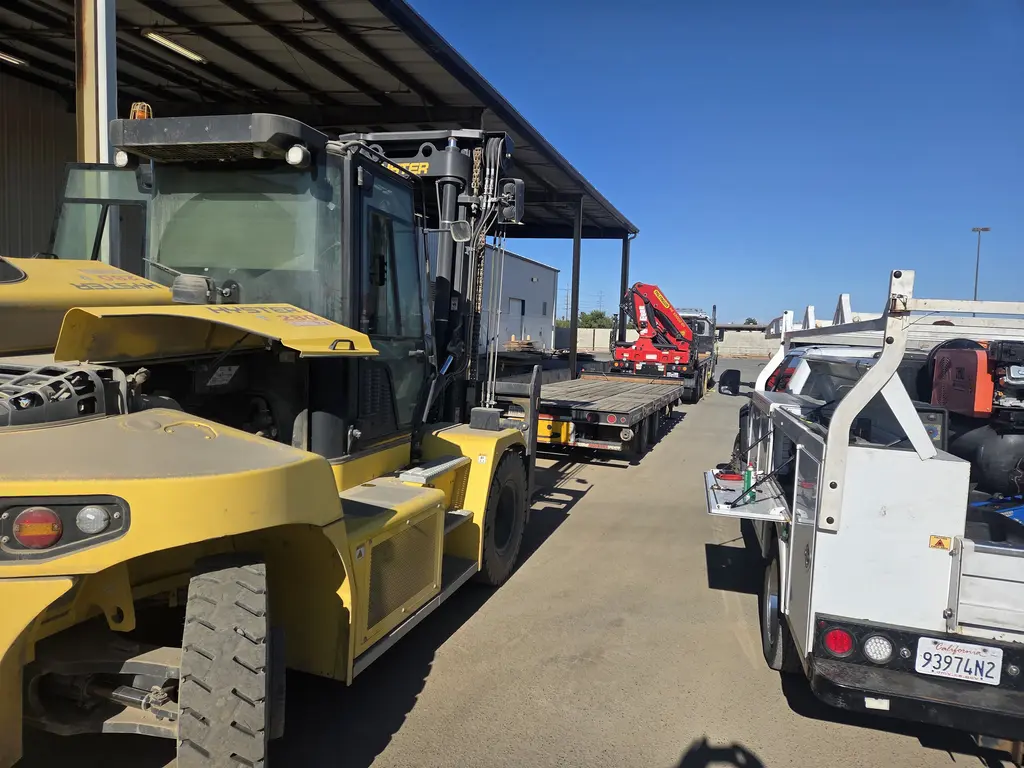 Heavy forklift and flatbed knuckle boom truck in a fleet yard