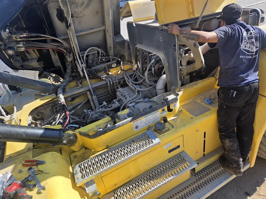 ADE technician working in the open engine bay of a yellow piece of heavy equipment