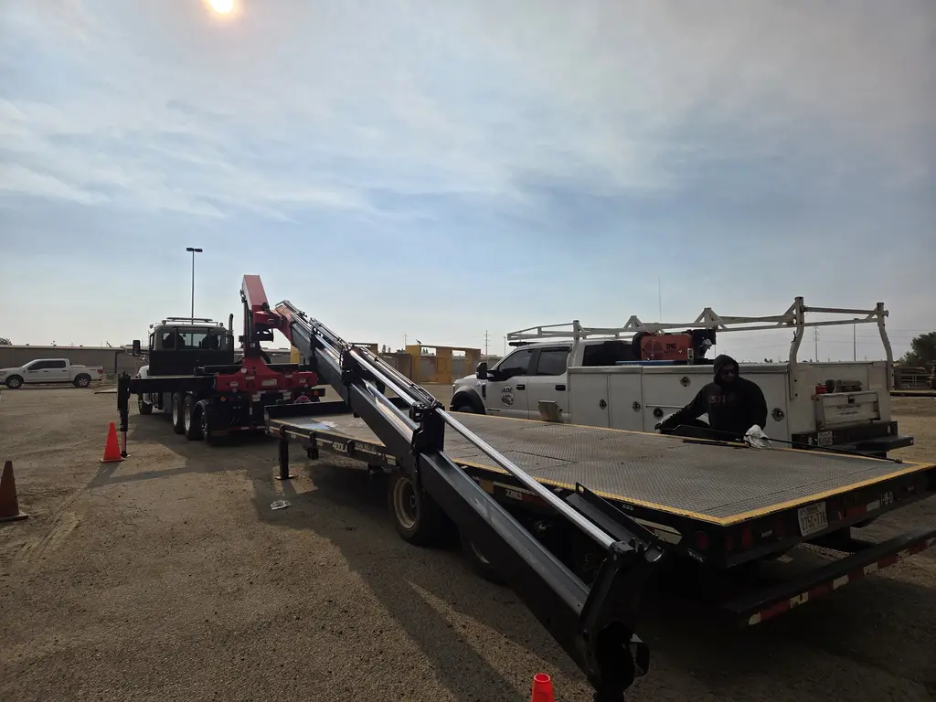 ADE technician working the hydraulics of a knuckle boom crane on a flatbed at dusk