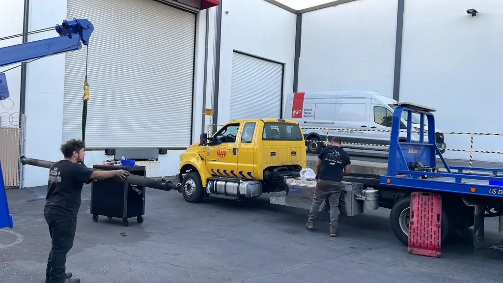 Two ADE technicians pulling a driveshaft from a tow truck on site