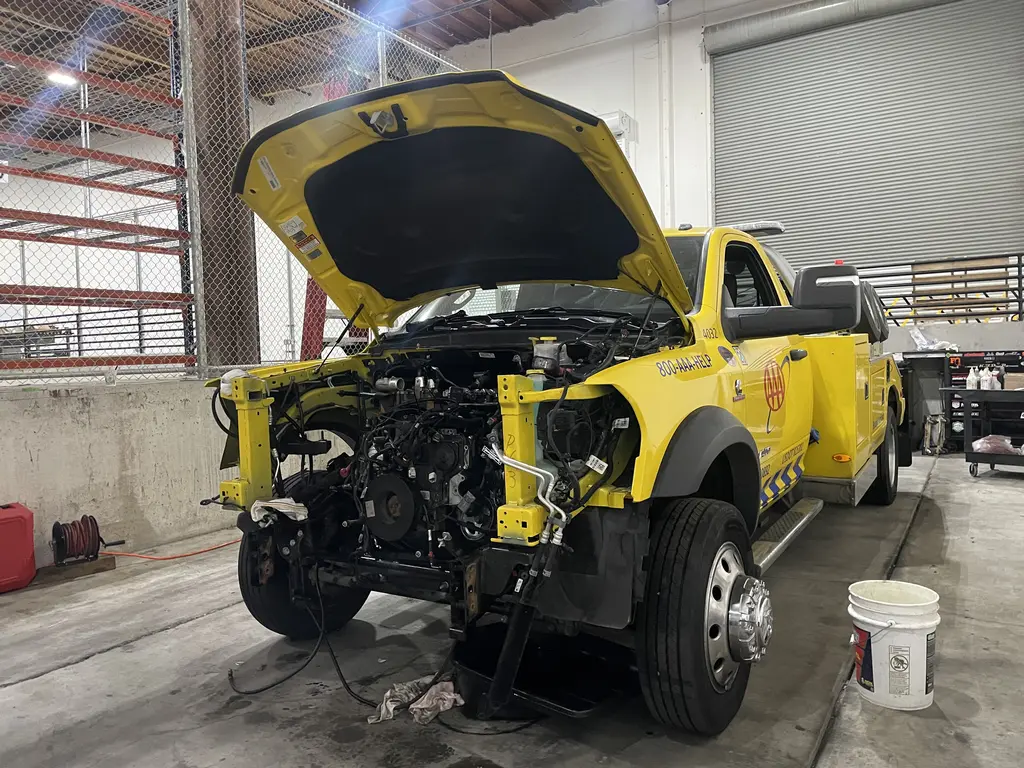 Yellow tow truck with the hood open and front end taken apart for diesel engine repair